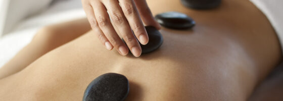 Hands massaging lower back with warm stones. You may also like: